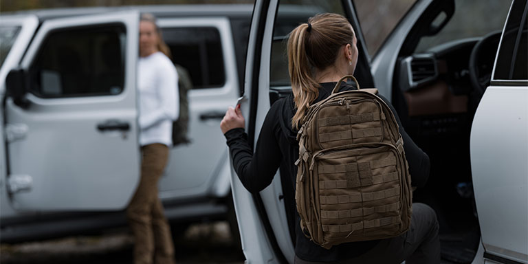 woman with ponytail and long sleeve shirt with backpack steps on vehicle's running board