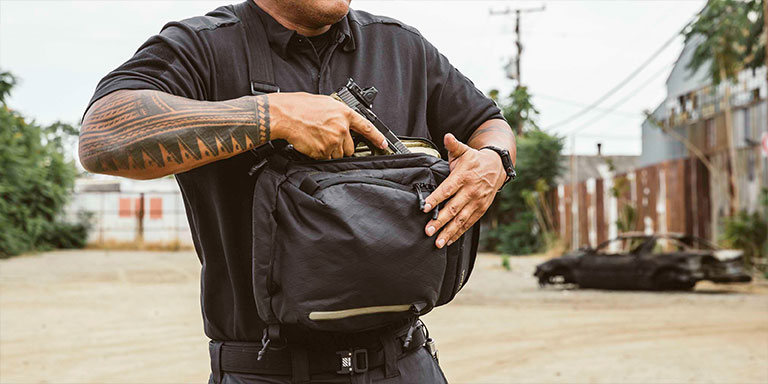 man with tattoos draws concealed handgun from conceal carry sling bag