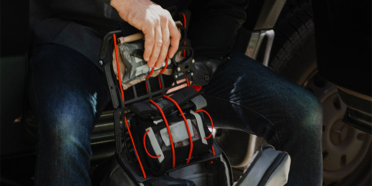 Man pulls organization system out of backpack with various survival gear attached.