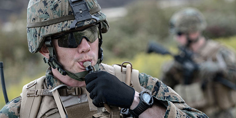 Man in military kit drinks from hydration pack.