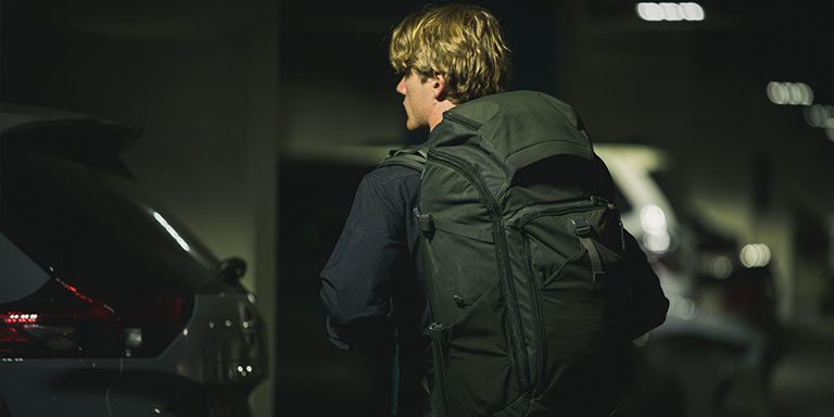Man with laarge backpack walks through parking garage.