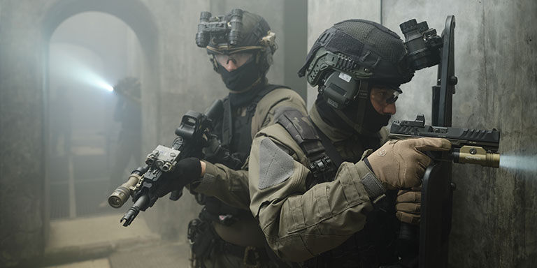 Multiple men in tactical gear with illuminated weapon lights clear a building