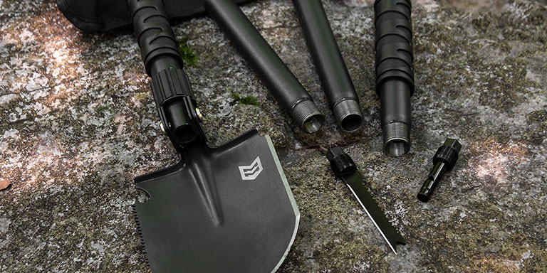 Modular shovel with built in compass and firestarter taken apart laying on rock