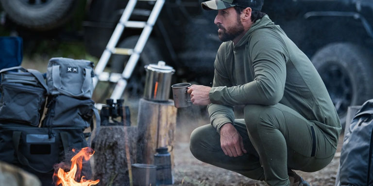 Man dressed in base layers by campfire