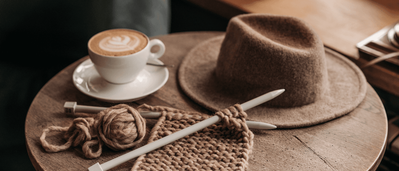 Brown handspun yarn on a table with coffee and hat