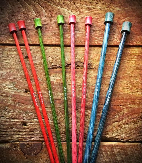 Wooden Knitting Needles Set by Knitters Pride Dreamz, featuring 10" & 14" lengths in red, green, pink, and blue on a rustic wooden background.