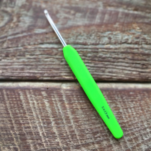 Knitters Pride Waves Crochet Hook on a wooden surface with ergonomic lime green handle and silver metal tip.
