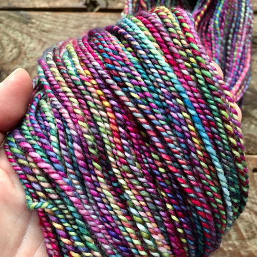 Luxury Handspun Merino Wool Yarn Rainbow Fiesta, a vibrant multicolored skein, featuring pink, purple, blue, and yellow hues, made from 100% merino wool, by Forever Winding Wool.