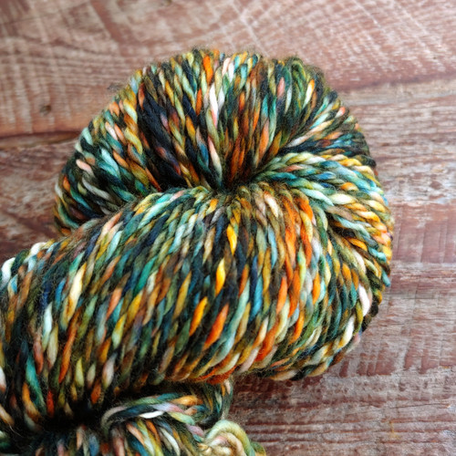 Luxury Merino wool yarn skein in Mountain Twilight, green, orange, and white hues, light worsted weight DK, showcasing multicolored variegated texture.