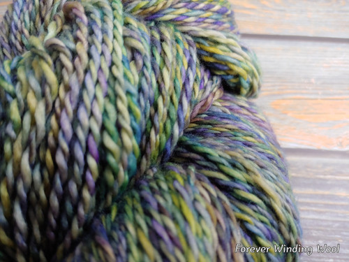 Multicolored yarn with shades of purple, blue, green, and yellow, sitting on a wooden surface.