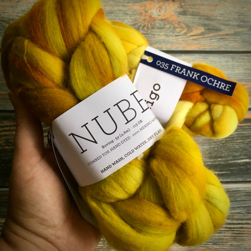 Malabrigo Nube Frank Ochre Merino Wool Roving, 4oz, yellow and orange hues, held in a hand against a wooden background.