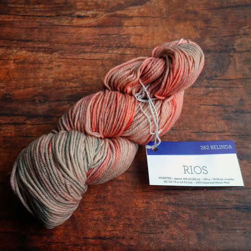 Malabrigo Rios RIO-262 Belinda Superwash Merino Worsted Yarn skein with label, showcasing multi-tonal pink and beige hues on a wooden surface.