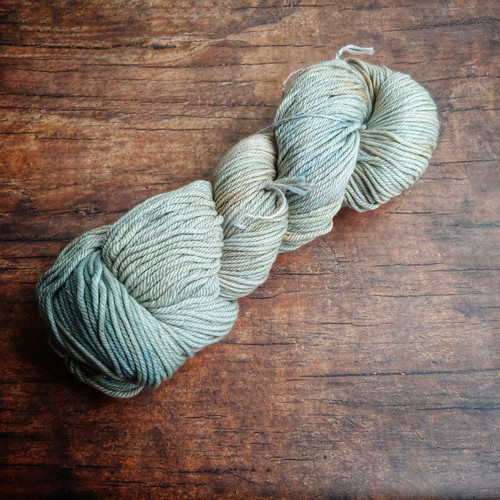 Malabrigo Rios Magnolia 263, Neutral Worsted Merino Yarn skein in a soft, creamy white hue, neatly arranged on a wooden surface.