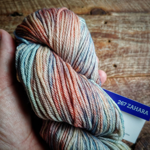 Malabrigo Rios RIO-267 Zahara Superwash Merino Worsted Yarn, multicolored yarn skein with orange, blue, and gray tones, held in a hand.