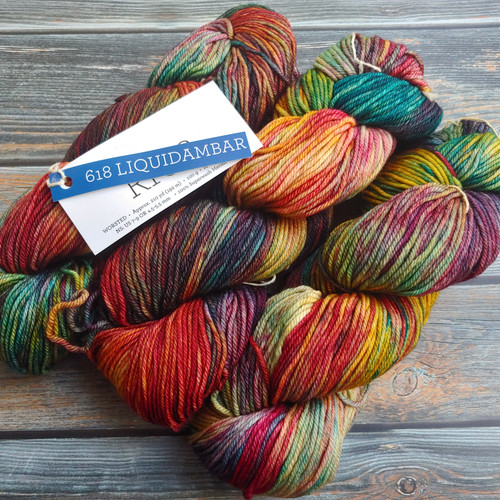 Malabrigo Rios Liquidambar yarn, a warm rainbow superwash merino yarn, featuring a multicolored skein with shades of red, orange, yellow, green, and purple, displayed on a wooden background with a label reading 618 Liquidambar. Malabrigo Rios Liquidambar yarn, a warm rainbow superwash merino yarn, featuring a multicolored skein with shades of red, orange, yellow, green, and purple, displayed on a wooden background with a label reading 618 Liquidambar.