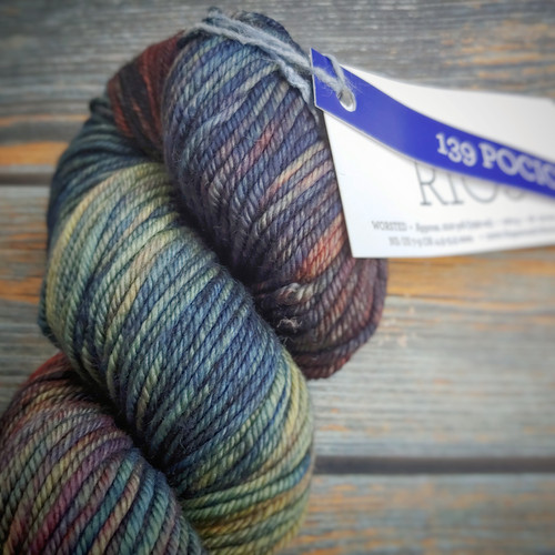 Malabrigo Rios Pocion yarn, a deep jewel-toned multicolor merino wool skein with shades of blue, green, and orange, neatly wrapped with a tag, showcasing the brand's signature color palette and texture. Malabrigo Rios Pocion yarn, a deep jewel-toned multicolor merino wool skein with shades of blue, green, and orange, neatly wrapped with a tag, showcasing the brand's signature color palette and texture.