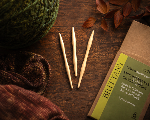Brittany Birch Wood Cable Needles, 3-piece handcrafted knitting notions set in birch wood, displayed with packaging and yarn.