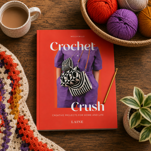 Crochet Crush book with creative projects for home and life, by Laine, on a wooden table with colorful crochet items nearby.