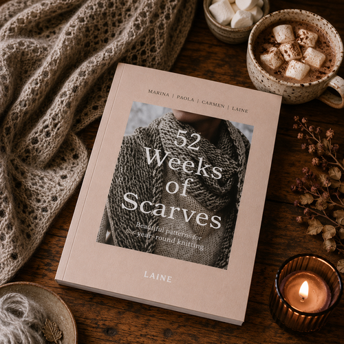 52 Weeks of Scarves book by Laine, beige cover with white text, black and white scarf, surrounded by cozy knitting accessories and warm beverages.