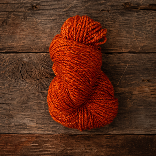 Twisted skein of orange bittersweet handspun yarn laying on a rustic wood table.