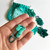 Teal stitch markers in a hand, with a Mindful Collection pack and scattered markers on a white background, showcasing the Mega Pack.