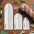 The Sock Ruler, set of three white plastic measuring gauges with black markings, in various sizes, on a wooden surface with yarn and flowers.