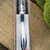 Ergonomic crochet hook with curved grip, navy and white handle, packaged on beige fabric with green yarn, Swing Maxi Ergonomic brand crochet tool.
