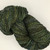 Blue Spruce Artisan Merino Wool Yarn, Sport/DK, made from high-quality merino wool in dark green with yellow and blue tones,  skein on white background, by Forever Winding Wool.