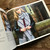 Malabrigo Book 13 Shawl Road, woman wearing gray scarf with dark blue stripes, black jacket, and jeans, leaning on wooden railing.