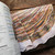 Malabrigo Book 13: Shawl Road, colorful striped shawl on white background in a book on wooden table, showcasing multicolored yarn pattern.