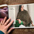 Malabrigo pattern book #17 Ponchos & Familia, woman wearing green poncho, holding yarn skeins on wooden table.