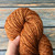 Handmade Art Yarn - Butterscotch Merino, DK Weight, golden brown yarn skein with subtle sheen, held by a hand against a wooden background.
