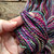 Luxury Handspun Merino Wool Yarn - Rainbow Fiesta, a multicolored skein with pink, purple, blue, green, and yellow hues, handspun merino wool, Forever Winding Wool brand.
