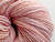 Forever Winding Wool Artisan Merino Wool Yarn in Pink Opal, a skein of soft pink, peach, and purple variegated yarn with a subtle sheen, showcasing its gentle color blend and textured threads.