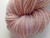 Forever Winding Wool Artisan Merino Wool Yarn in Pink Opal, a soft pink and white marled skein with subtle purple undertones, showcasing the yarn's texture and color blend in a neatly wrapped bundle.