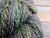 Multicolored yarn with shades of purple, blue, green, and yellow, sitting on a wooden surface.