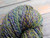 Multicolored yarn with shades of purple, blue, and yellow, on a wooden surface, neatly coiled and twisted.