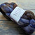 Malabrigo Nube Cirrus Gray, Merino Wool Roving, 4oz, spinning & felting fiber, gray, brown, purple hues, labeled NUBE, on wooden surface.