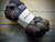 Malabrigo Nube Cirrus Gray, 4oz Merino Wool Roving, soft gray-brown hues, braided skein with white label on a wooden background.