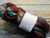 Malabrigo Nube - Corteza, 100% Merino Wool Roving, 4oz, multicolored yarn in shades of brown, green, and beige, wrapped in white label.