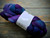 Malabrigo Nube Whales Road 100% Merino wool roving, 4oz bundle of vibrant purple and blue hues, rustic wooden background, ideal for spinning and felting Merino wool fiber.