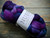 Malabrigo Nube Whales Road 100% Merino Wool Roving, 4oz, purple and blue hues, suitable for hand spinning and felting, on rustic wooden background with white wrap.
