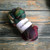 Malabrigo Nube Arco Iris 4oz merino wool roving, multicolor shades of green, purple, and pink on a wooden background, spinning, and felting fiber for crafters, Malabrigo brand yarn.