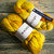 Malabrigo Nube Frank Ochre, Merino Wool Roving, two 4oz skeins, yellow, malabrigo label, on wooden surface.