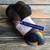 Malabrigo Nube Candombe merino wool roving, 4oz, multicolored skein with purple, blue, green, and brown hues, wrapped in white and blue label.