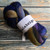 Malabrigo Nube Candombe merino wool roving, 4oz, in dark blue, purple, and brown hues, wrapped in white label on rustic wooden background.