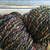 Kimball Coal Dust Artisan Handspun Bulky Merino Yarn, multicolored with black base, displaying shades of pink, green, blue, and orange.
