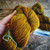 Malabrigo Rios Glitter yarn in color 048, a warm golden brown worsted weight superwash Merino wool skein with subtle sparkle, held in a hand.