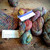 Malabrigo Rios Queguay multicolor worsted merino yarn skeins in various colors on a wooden surface, labeled "Rios" and showing yarn samples.