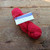 Malabrigo Worsted Geranio yarn, a vibrant red, hand-dyed merino wool skein with label, on wooden surface, showcasing bold color and texture.
